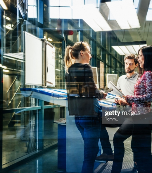 A team of engineers having a discussion at a desk in a large printing factory.